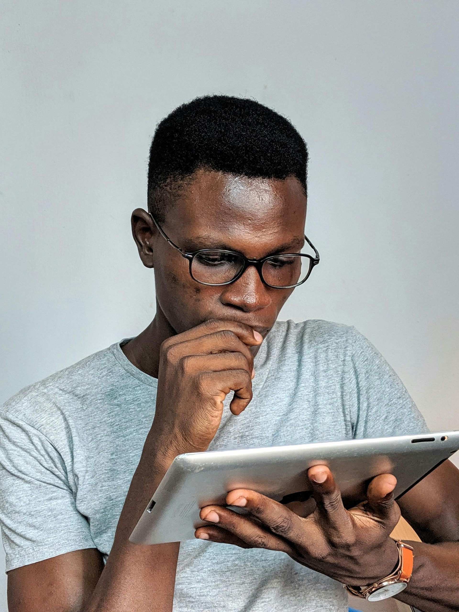 Young man wearing glasses engrossed in using a tablet device indoors.